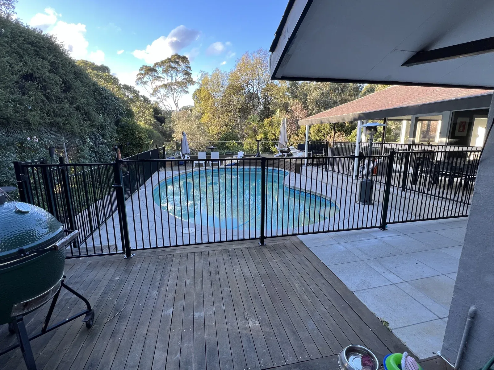 Timber deck beside a swimming pool with garden and surrounding trees