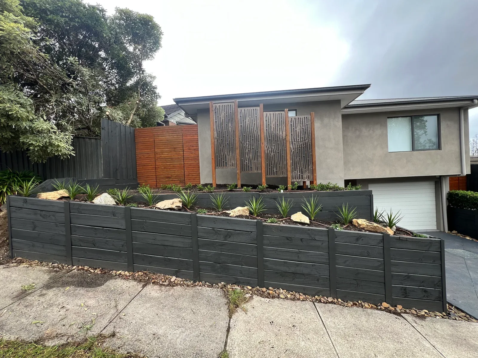 Charcoal sleeper retaining walls with layered planting, feature rocks and decorative timber screens
